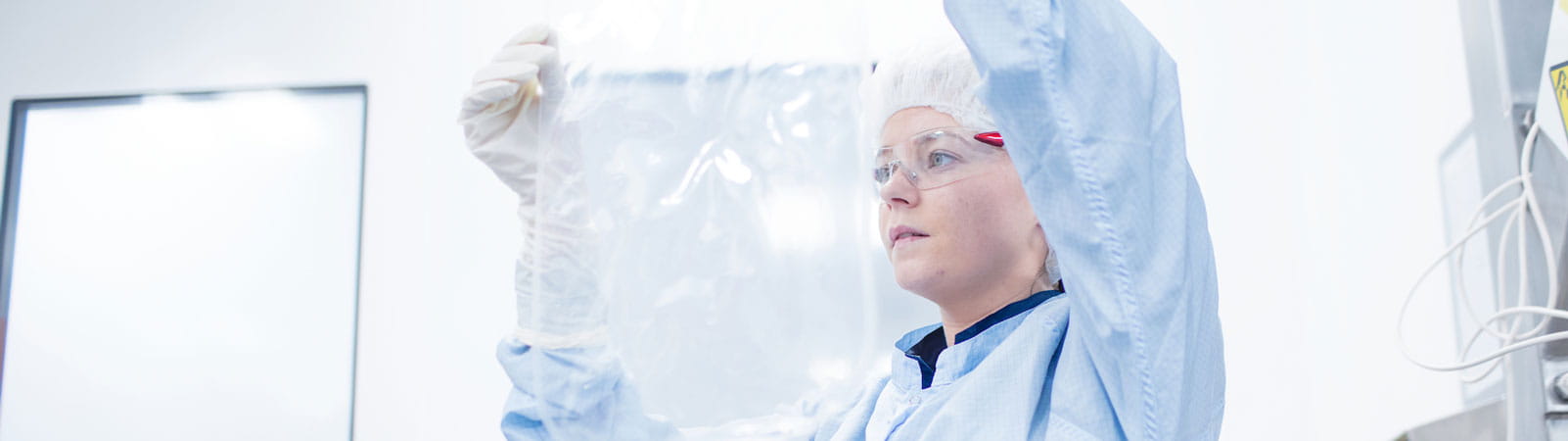 Technicien manipulant un grand sac transparent dans un environnement stérile dans le cadre de la production des vaccins grippe